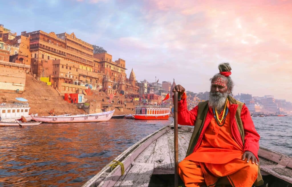 Homem indiano faz um passeio de barco no rio Ganges com vista para a arquitetura histórica da cidade de Varanasi ao pôr do sol.