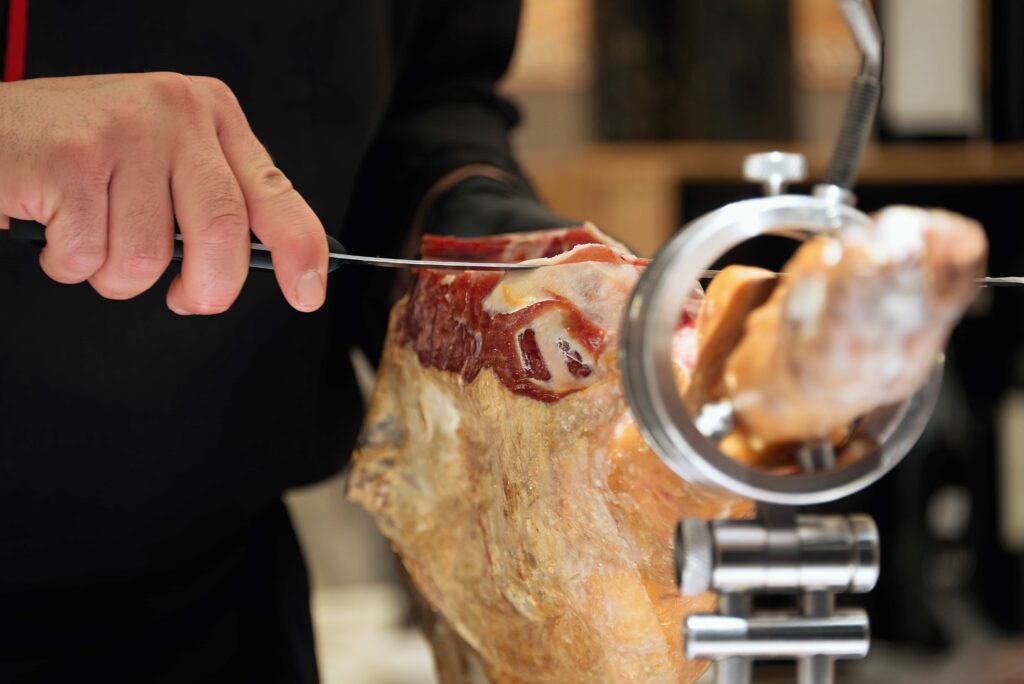 Mãos de homem cortando uma peça de Jamón serrano.