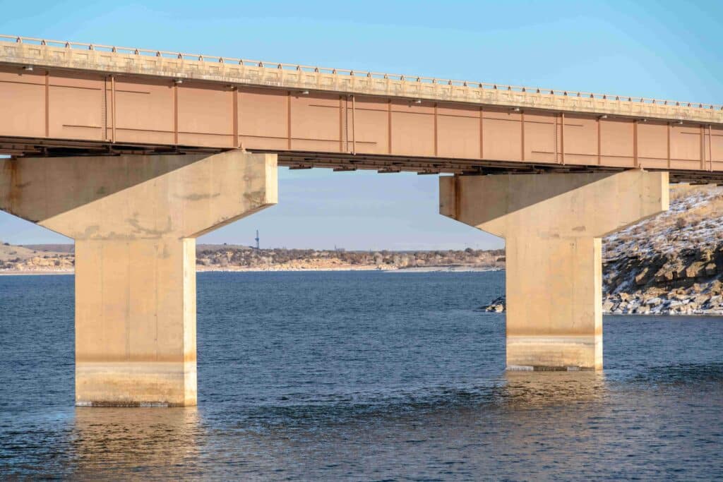 Foco em uma ponte de viga apoiada por pilares sobre o lago azul contra o céu nublado.
